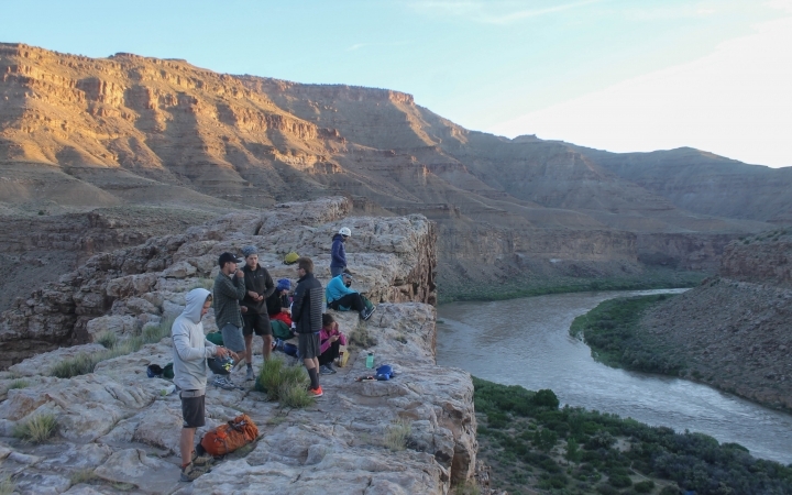 A group of outward bound gap year students gather on a high cliff above a canyon with a river flowing through it.